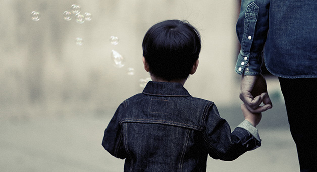 Image of a young child holding a hand and blowing bubbles