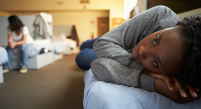 Image of two youth affected by homelessness in a shelter: one lying on a cot; one sitting on a cot
